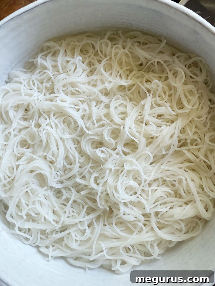 Cooked vermicelli noodles being placed into a large salad bowl as the base.