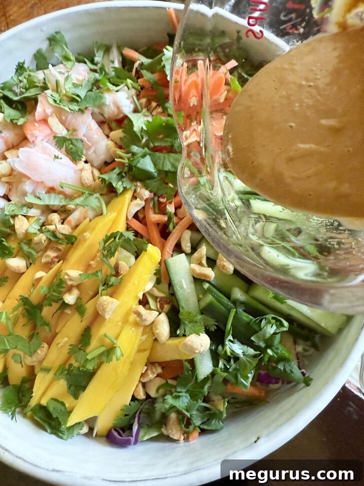 Pouring the Vietnamese peanut dressing generously over the colorful summer roll salad.