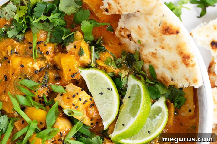 Chicken mango curry in serving bowl with naan bread.