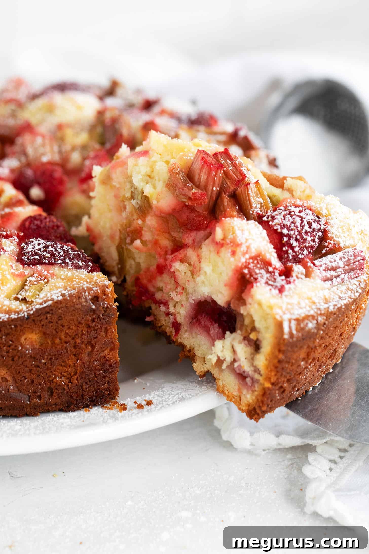 A beautifully baked and sliced strawberry rhubarb cake on a serving plate.
