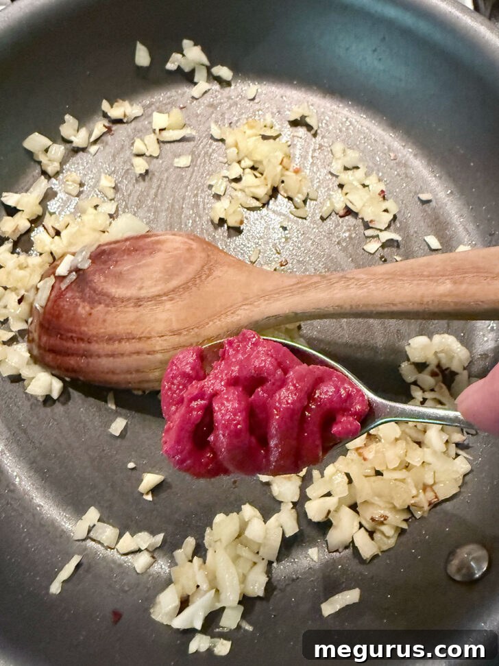 Adding tomato paste to the skillet with the sautéed onion and garlic.