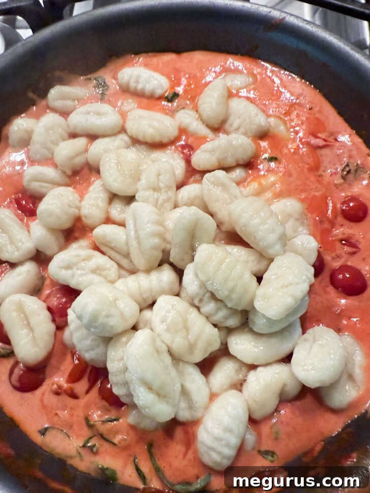Adding the cooked gnocchi to the skillet with the tomato cream sauce.