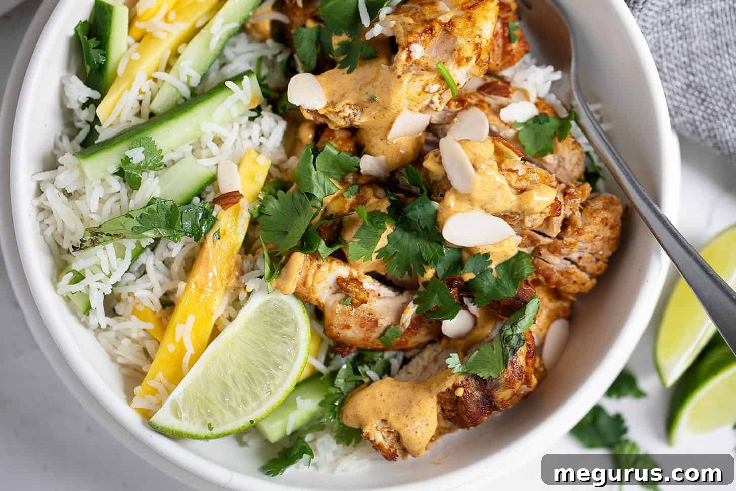 Coronation chicken rice bowl in a serving bowl with a fork, showing the vibrant ingredients.