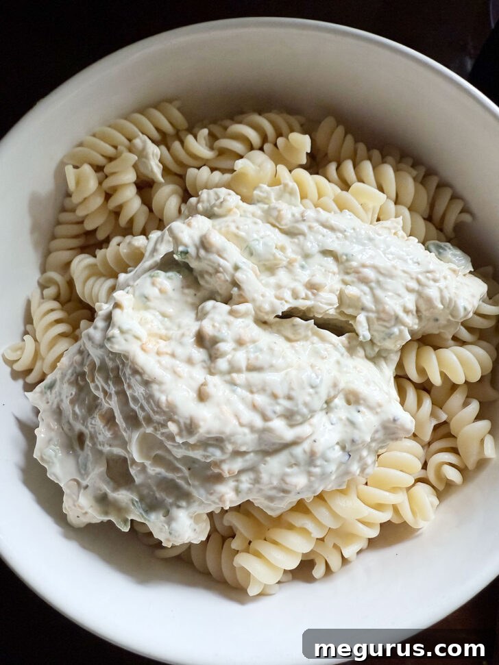 The creamy jalapeño popper pasta salad dressing being poured over the cooked pasta in a large mixing bowl.