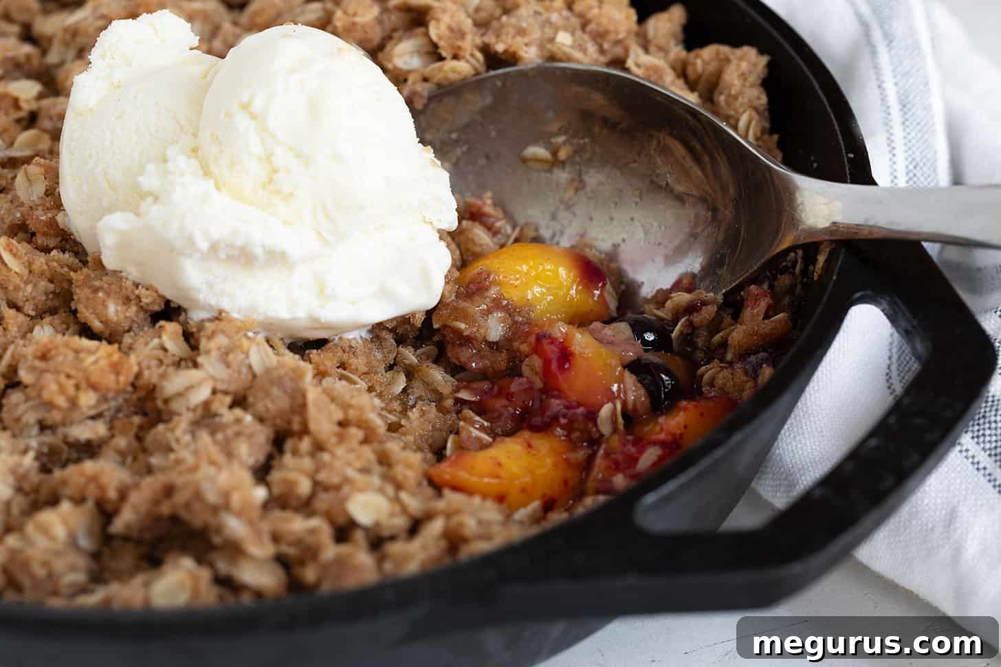Golden brown peach blueberry crisp bubbling in a rustic cast iron skillet, ready to serve.