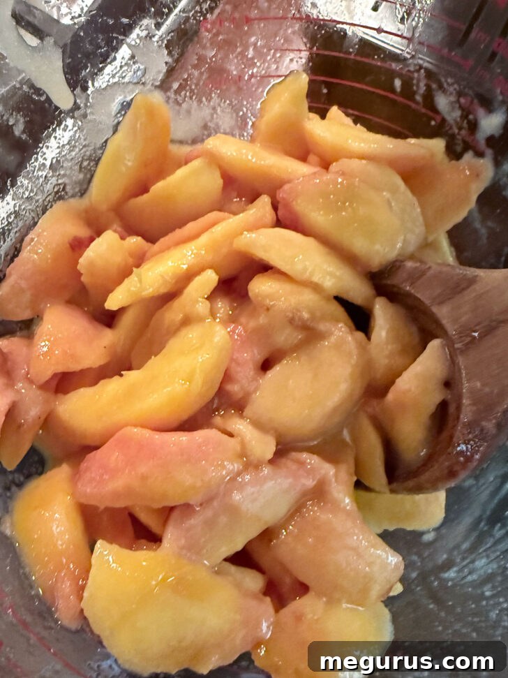 Sliced peaches mixed with sugar, cornstarch, water, and lemon juice in a bowl.