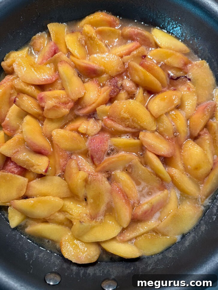 Peach mixture simmering gently in a large frying pan on the stovetop.