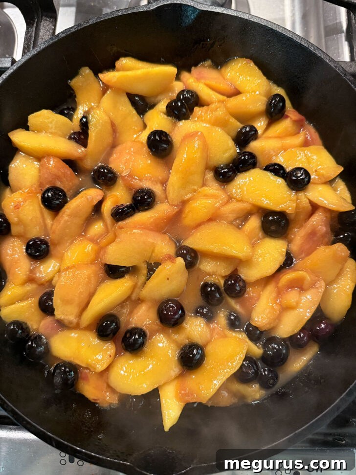 The finished peach and blueberry fruit filling, thick and syrupy, resting in a cast iron skillet.