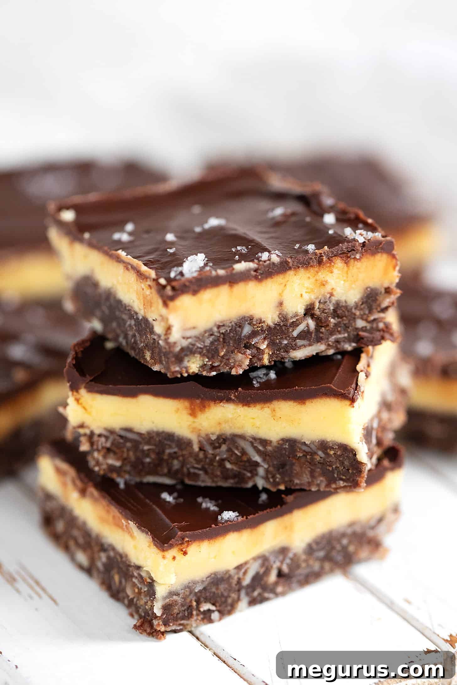 Elegantly cut and stacked Nanaimo bars presented on a wooden serving board, showcasing the three distinct layers: a crunchy base, a creamy yellow filling, and a glossy chocolate topping.