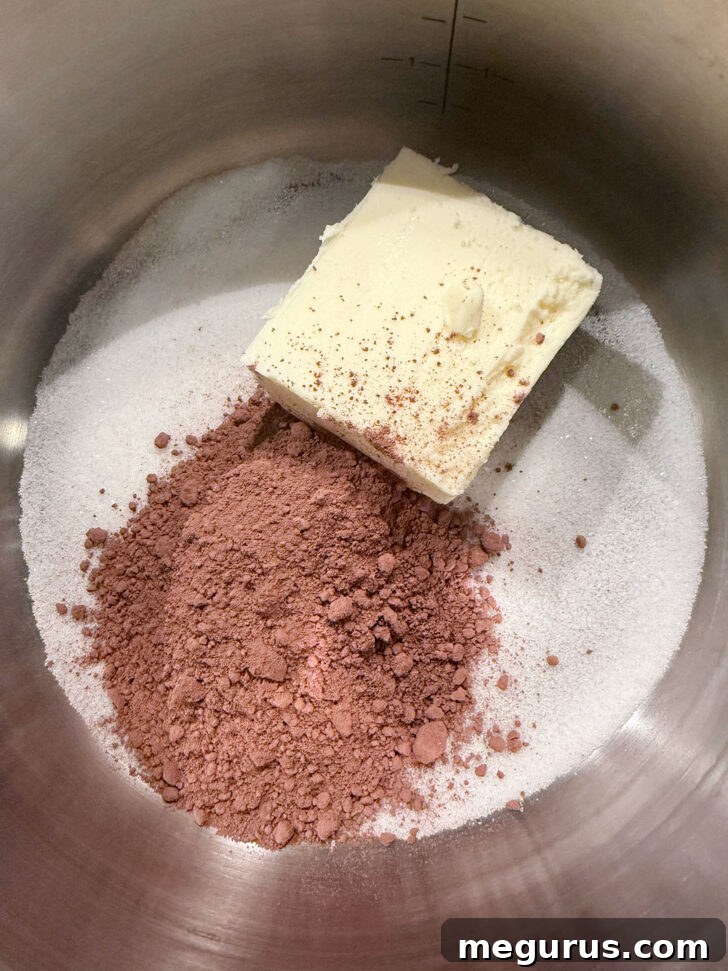 Butter, cocoa powder, and sugar melting together in a saucepan on the stovetop, forming the rich base layer for Nanaimo bars.