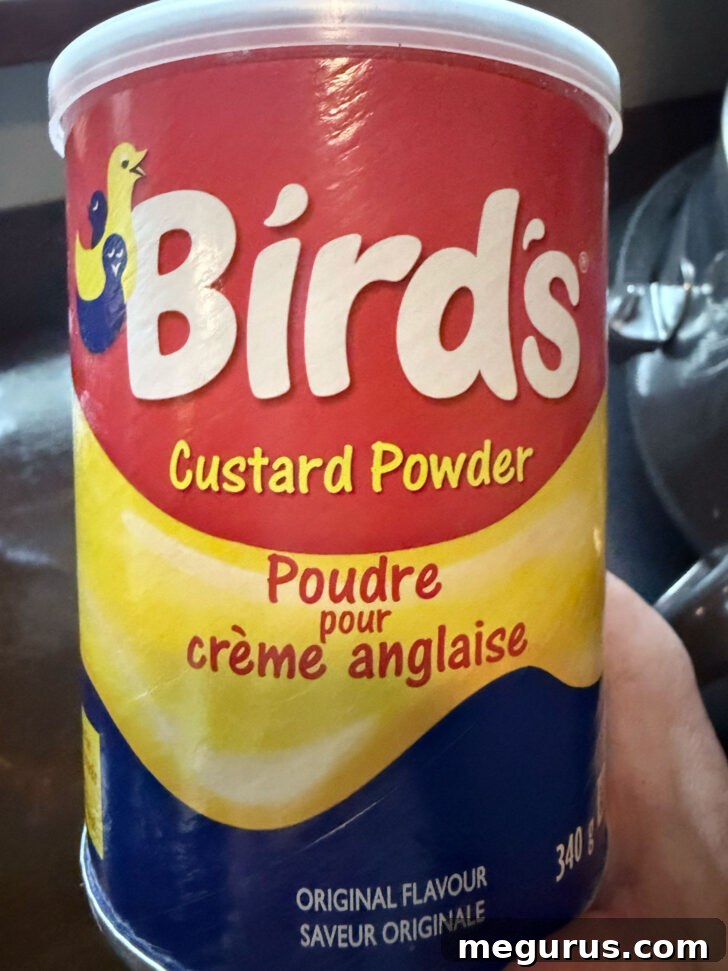 A bright red and yellow can of Bird's Custard Powder, signifying its use as the essential ingredient for the creamy filling layer.