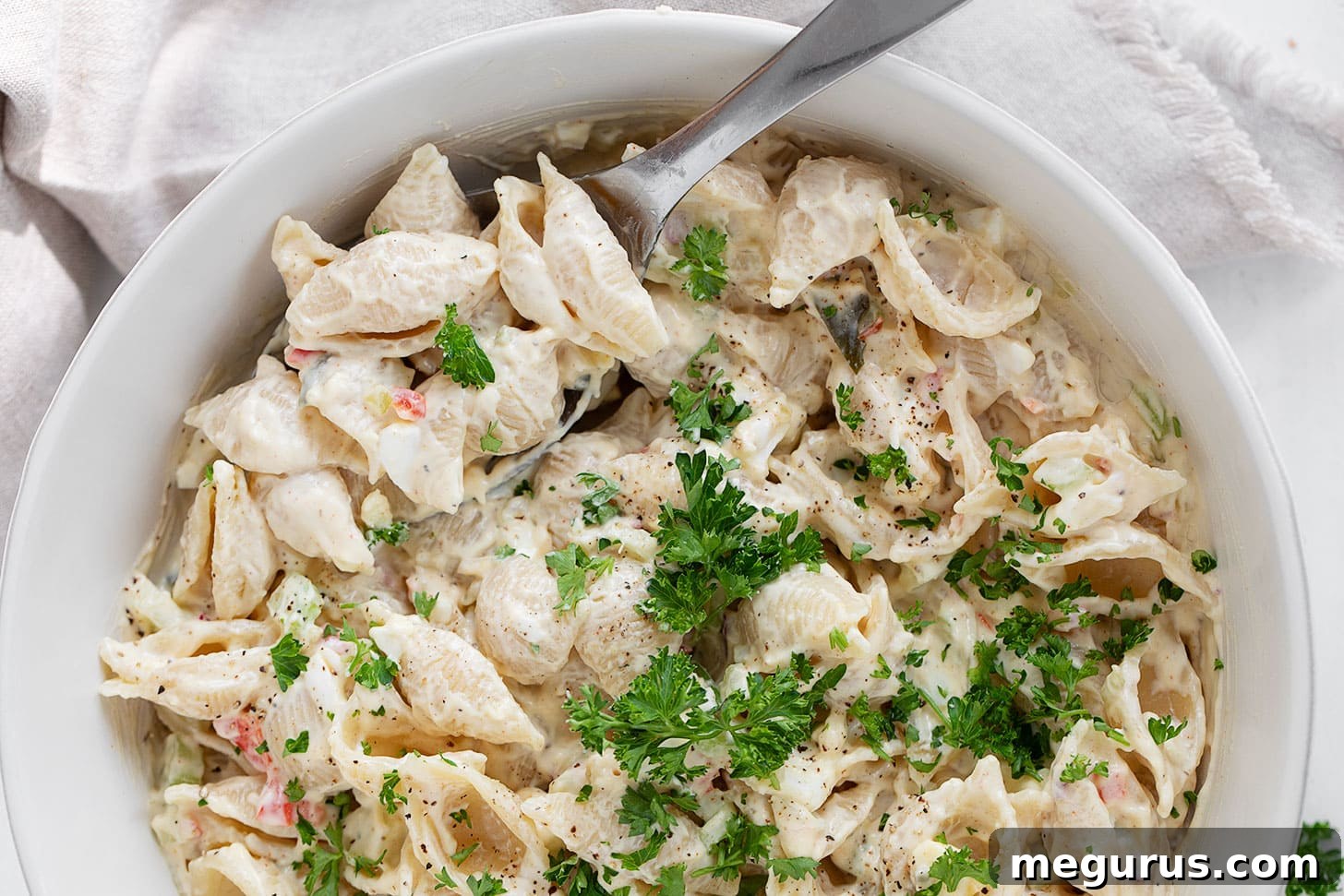 A large bowl of creamy shell pasta salad, garnished with fresh parsley, ready for serving at a summer gathering.