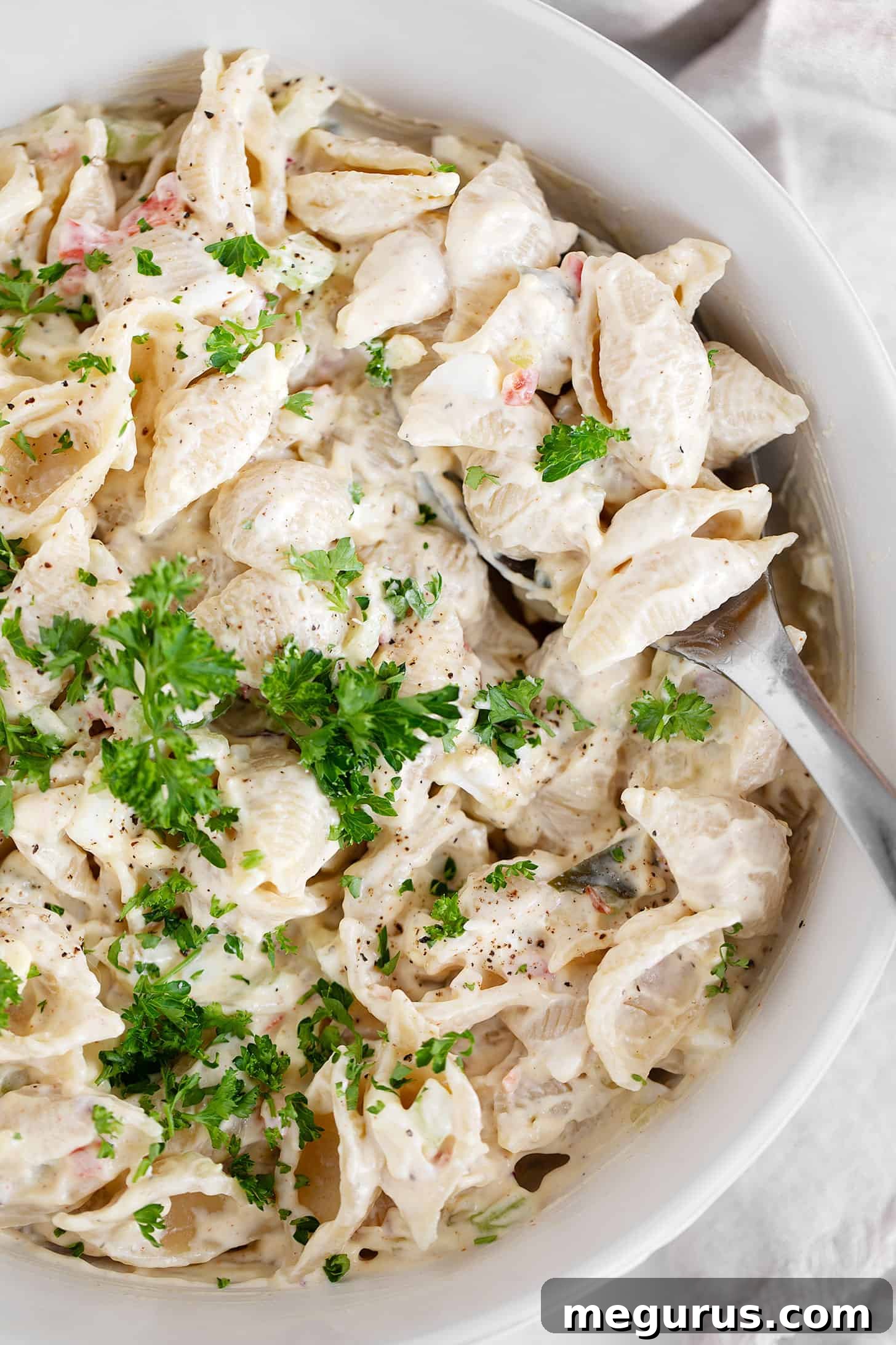 Close-up of creamy shell pasta salad in a large bowl, highlighting the texture and fresh ingredients.