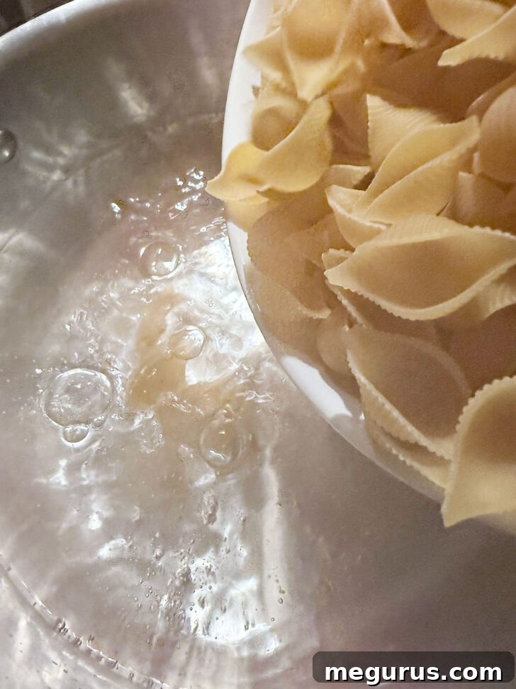 Shell pasta being added to a pot of boiling water on the stovetop.