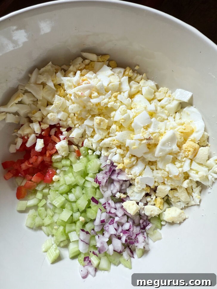 Chopped hard-boiled eggs added to the bowl with diced vegetables for the pasta salad.