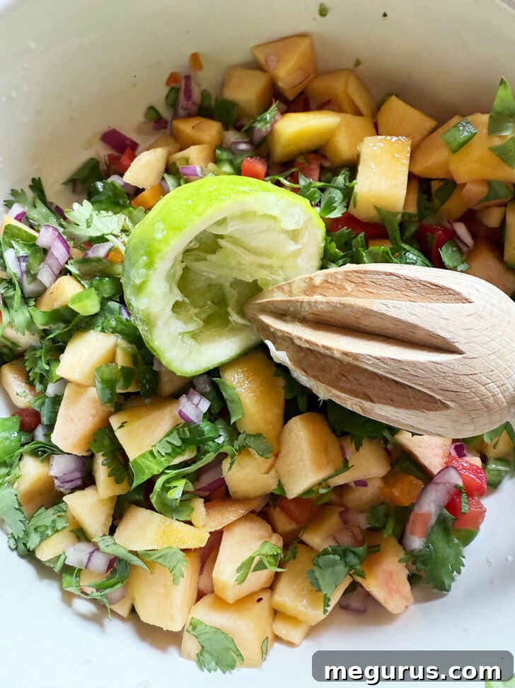 Fresh peach salsa ingredients in a bowl with a lime half and reamer.