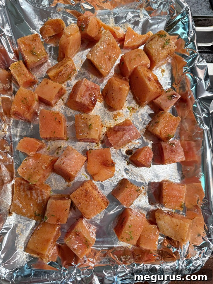 Seasoned salmon cubes spread onto a foil-lined baking sheet.