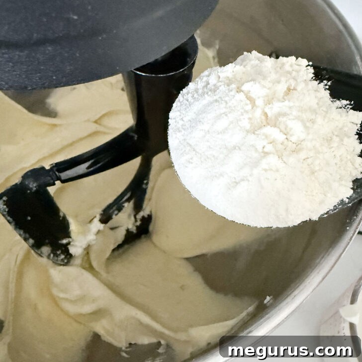 Adding flour to the batter in the mixing bowl.