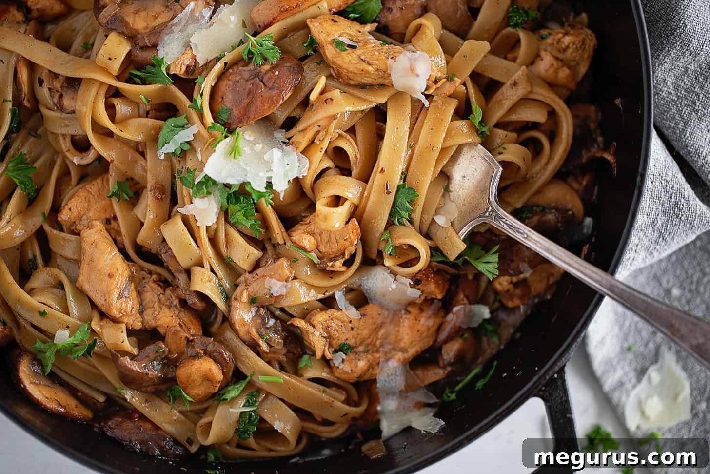 A close-up of creamy chicken Marsala fettuccine in a large skillet, ready to be served, with a fork resting on the side.