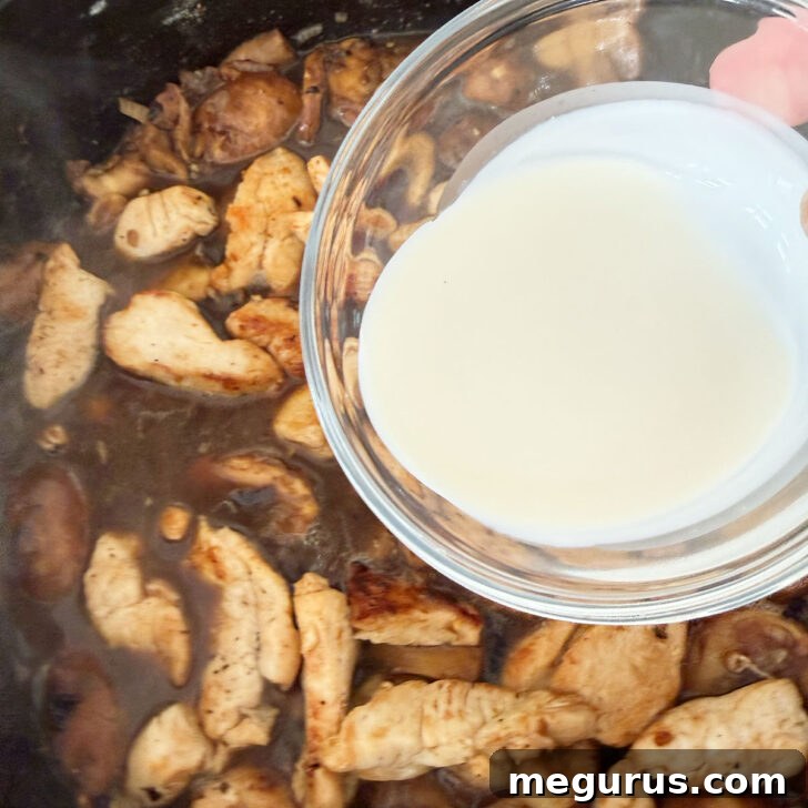 Rich heavy cream being stirred into the Marsala mushroom sauce in a skillet, creating a luxurious, velvety texture.