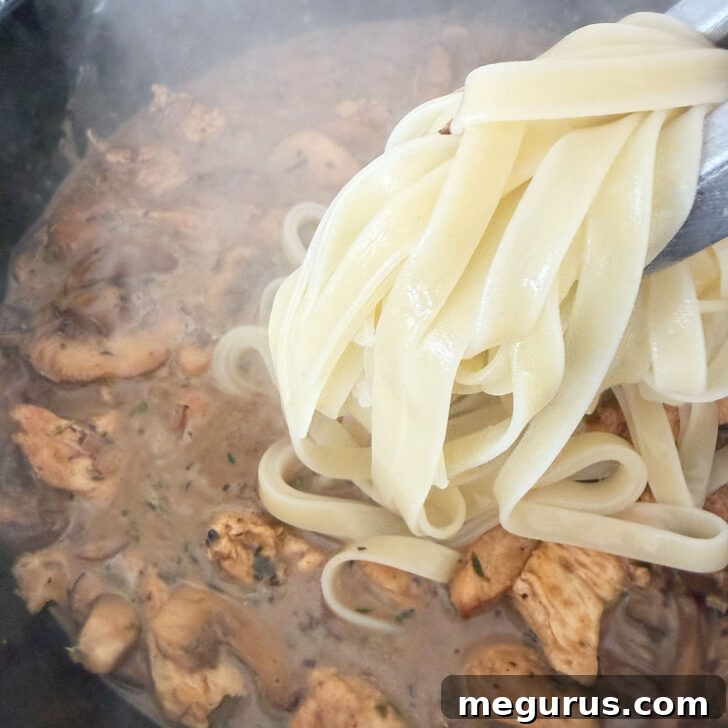 Al dente cooked fettuccine pasta being added to the creamy Marsala mushroom sauce in a skillet, ready to be tossed together.