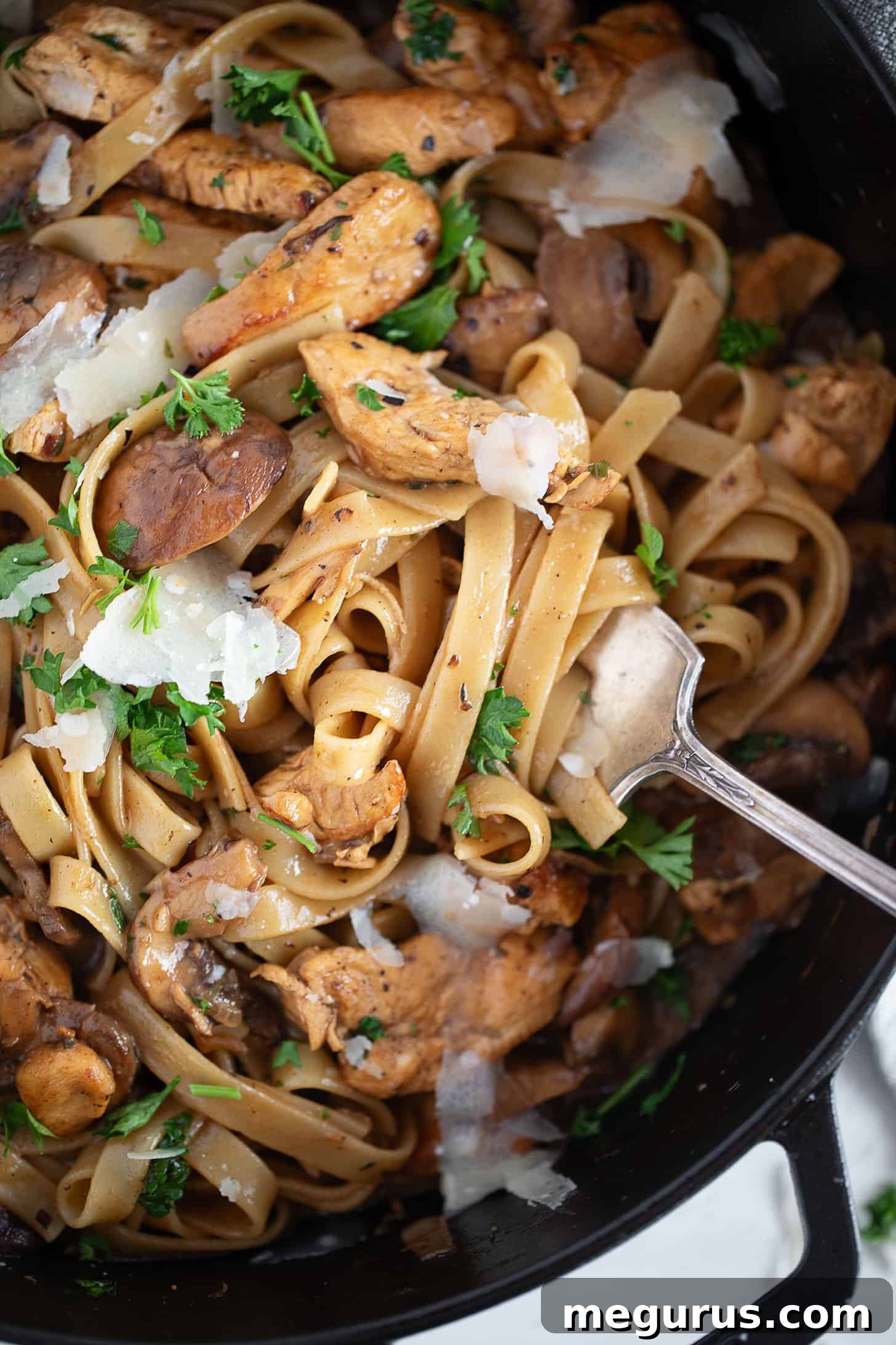 A vibrant and inviting close-up of creamy chicken Marsala pasta served in a large skillet, highlighting the rich sauce, tender chicken, and golden mushrooms. A fork is poised, ready for a delicious bite.