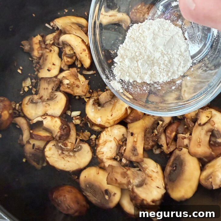 All-purpose flour being gently sprinkled over sautéed mushrooms and shallots in a skillet, forming the base for the rich sauce.