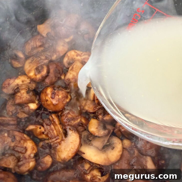 Pouring chicken broth into the simmering Marsala mushroom sauce in the skillet, adding depth to the rich liquid.