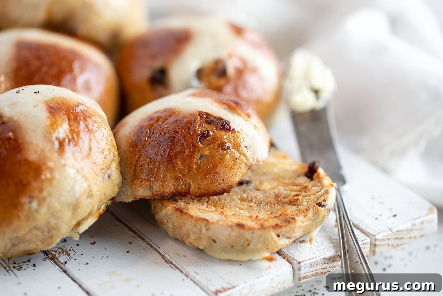 A selection of freshly baked Earl Grey hot cross buns, garnished with flour crosses and a glistening sugar glaze, arranged on a rustic wooden serving board.