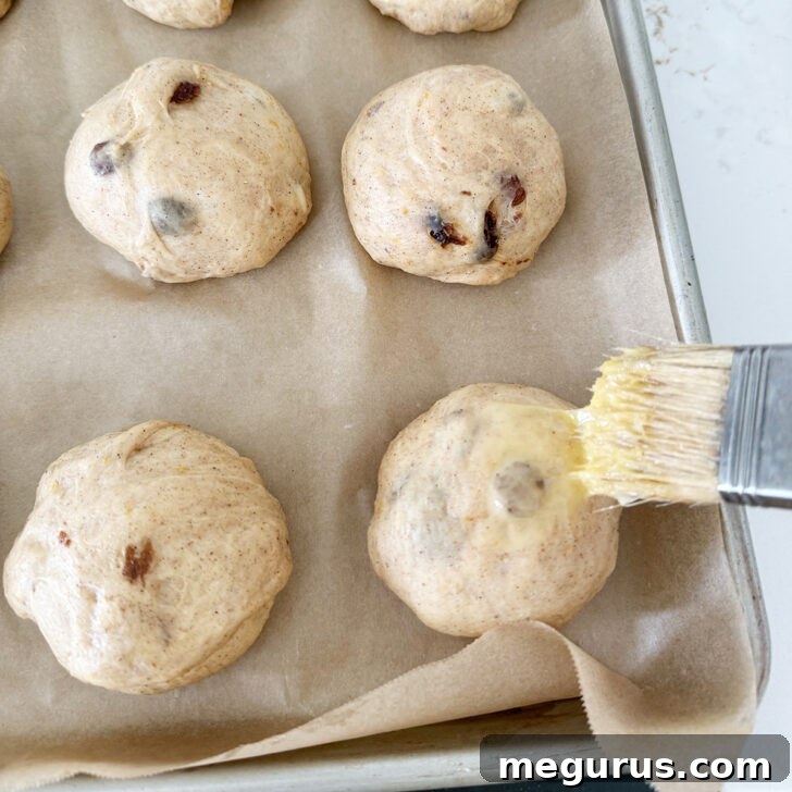 An egg wash is being carefully brushed onto the risen hot cross buns.