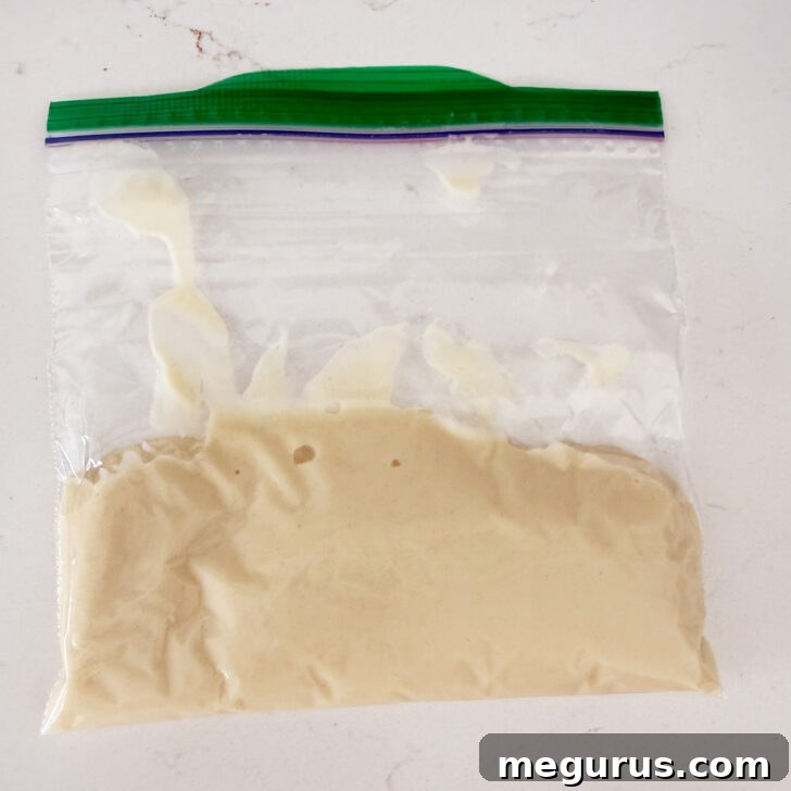 The flour cross mixture is contained within a plastic sandwich bag, with a corner snipped off.