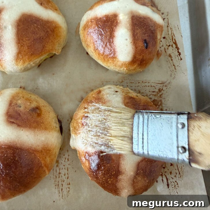 A brush applies a glossy sugar syrup to the hot, freshly baked Earl Grey hot cross buns.