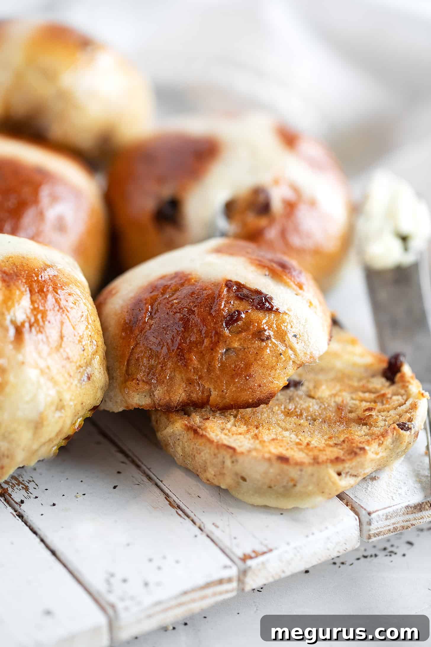 A close-up of a stack of golden Earl Grey hot cross buns, glistening with a sugar glaze and topped with flour crosses, on a wooden board.