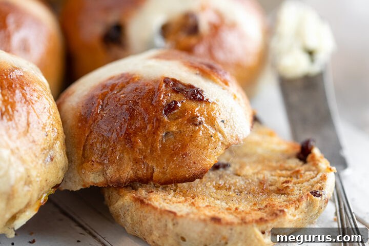 A serving of three Earl Grey Hot Cross Buns, beautifully glazed and crossed, arranged on a wooden board.
