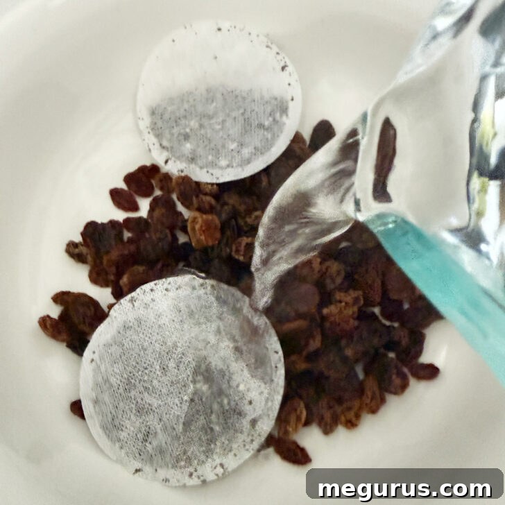 Boiling water is poured over sultana raisins and Earl Grey tea bags in a bowl.