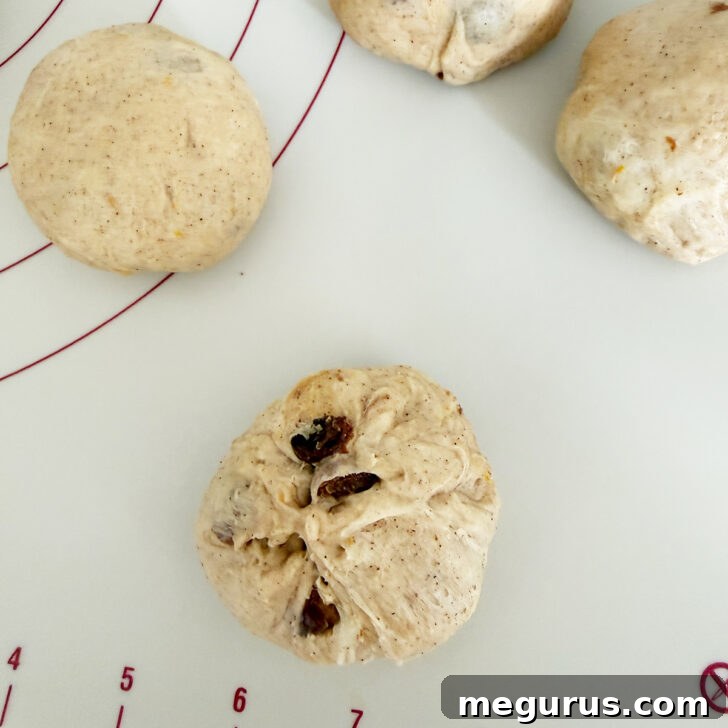 A hand is shaping a piece of dough into a smooth, round bun.