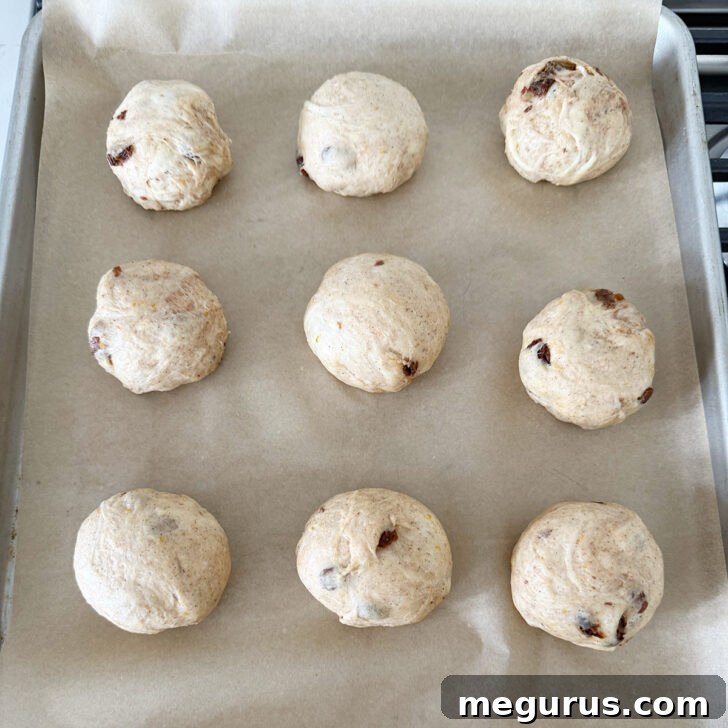 Shaped hot cross buns are neatly arranged on a parchment-lined baking sheet, spaced for rising.