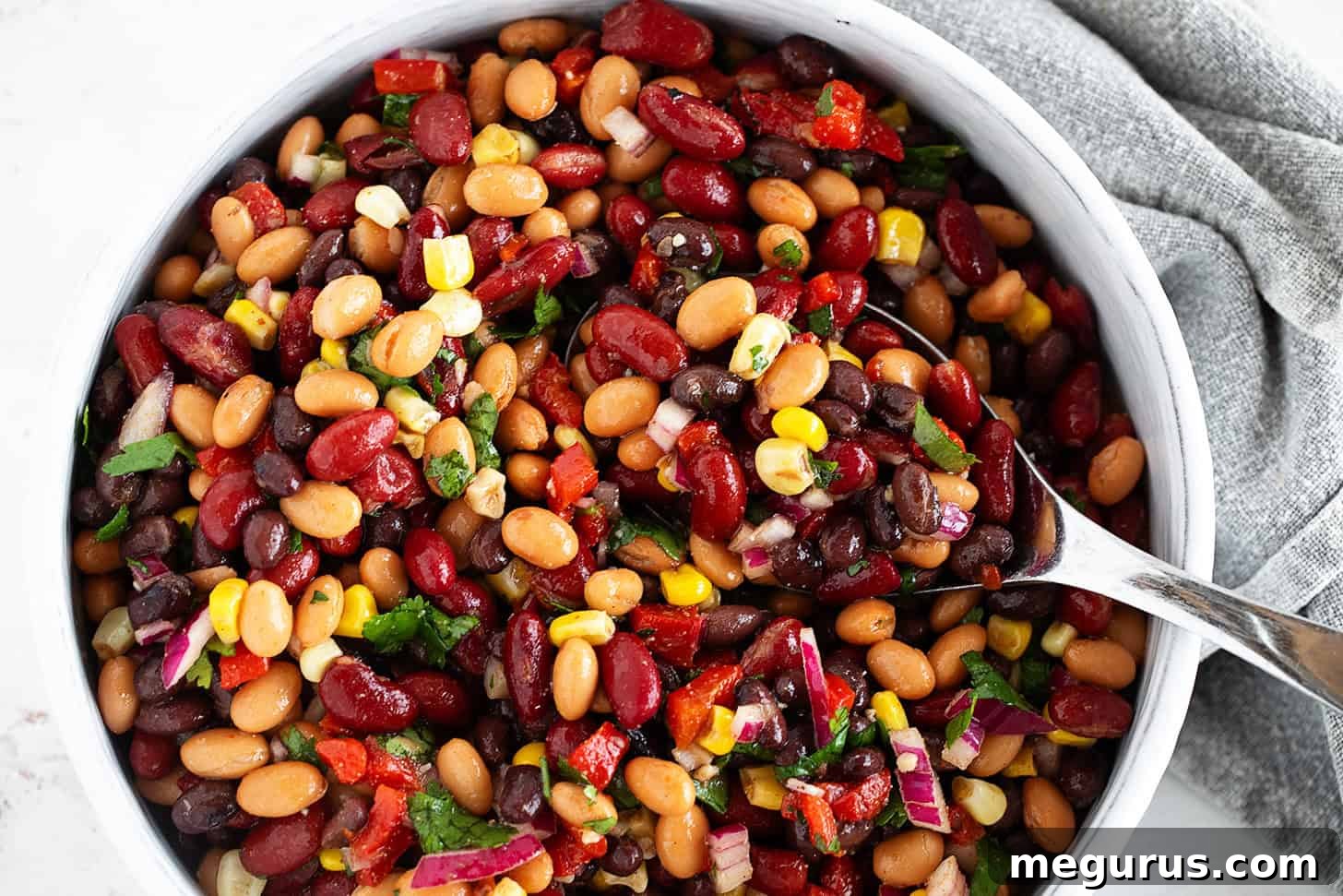 Mexican bean salad in a bowl with a large spoon.