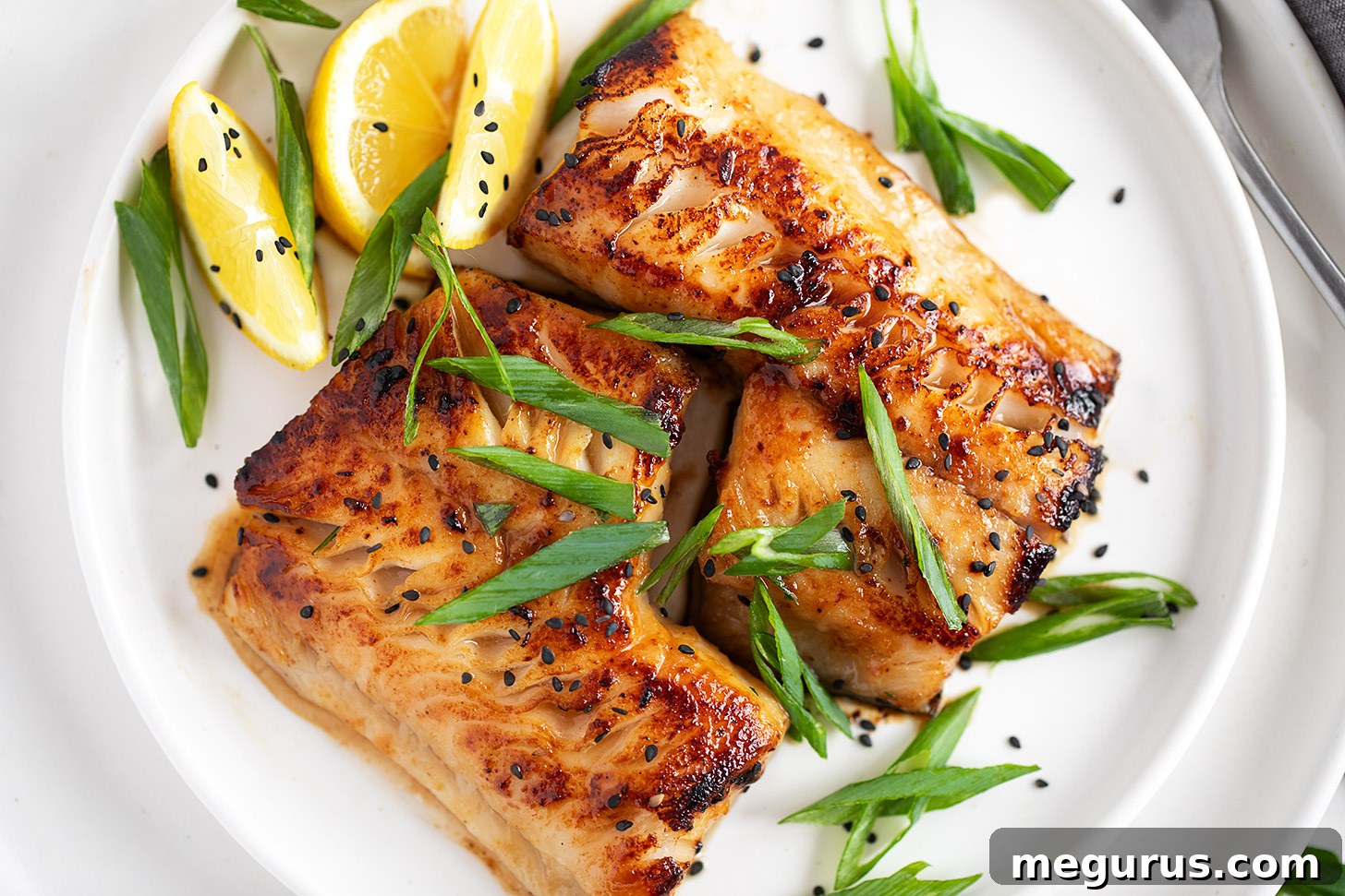Miso black cod on a serving plate with lemons and green onion.