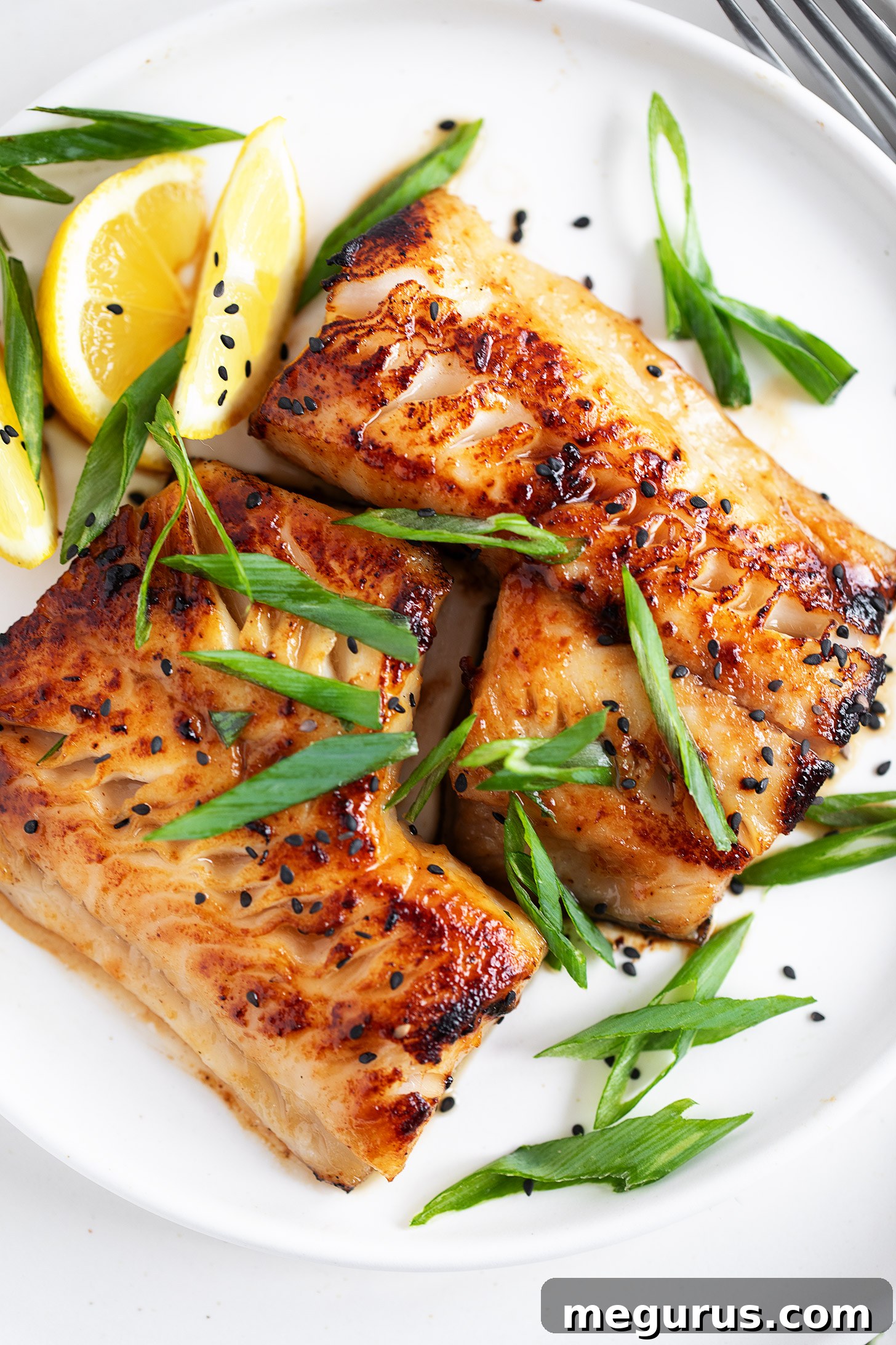 Miso black cod on a serving plate with lemons and green onion.