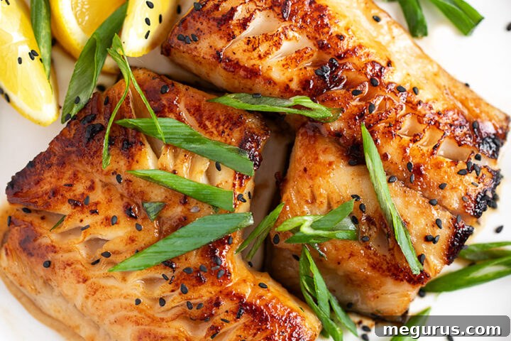 Miso black cod on a serving plate with lemons and green onion.