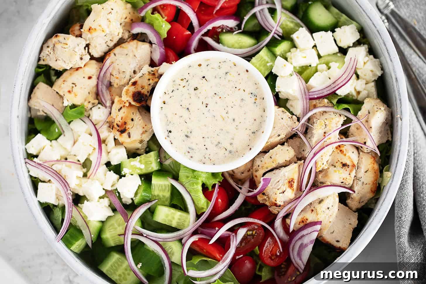 Grilled Chicken Souvlaki Salad with Tzatziki and Lemon Dressing 2 A close-up of a chicken souvlaki salad featuring grilled chicken, cherry tomatoes, cucumber, red onion, lettuce, feta cheese, and a small bowl of creamy dressing in the centre.