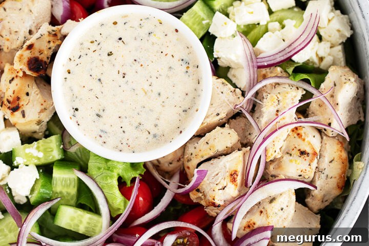 Grilled Chicken Souvlaki Salad with Tzatziki and Lemon Dressing 8 A close-up of a chicken souvlaki salad featuring grilled chicken, cherry tomatoes, cucumber, red onion, lettuce, feta cheese, and a small bowl of creamy dressing in the centre.